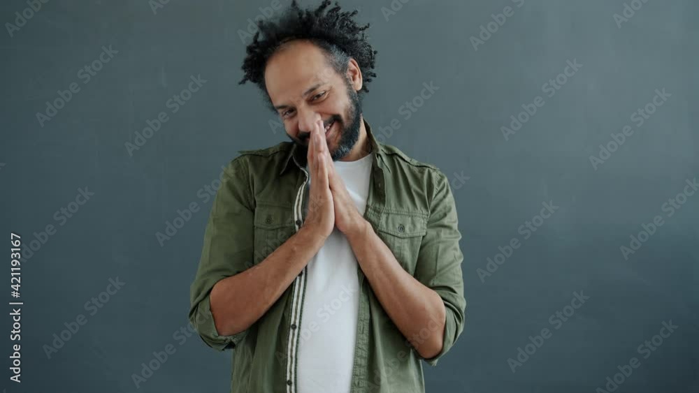 Portrait of shy mixed race man making heart shape with fingers and smiling modestly standing on gray background and looking at camera. People and romance concept. Portrait of shy mixed race man making heart shape with fingers and smiling modestly standing on gray background and looking at camera. People and romance concept.