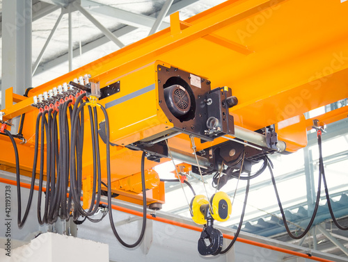Overhead crane inside factory or warehouse. That industrial machinery or lifting equipment consist of hoist, hook and wire rope traveling on beam girder structure. For manufacturing production plant.