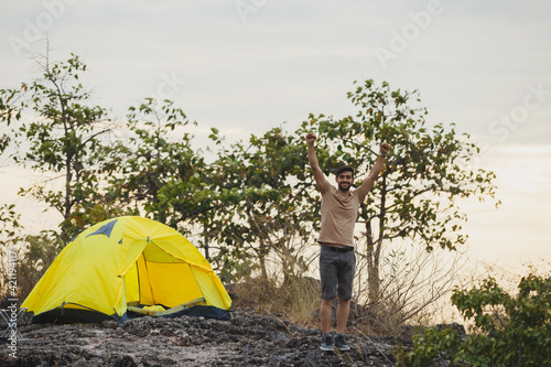 Handsome man freedom standing alone and hand up on mountain camping in forest with yellow tent. Travel forest concept.