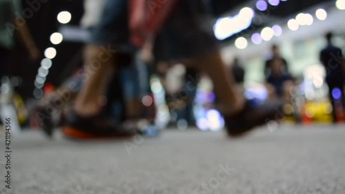 Defocused of ground level video clip of anonymous people walking while someone travel by wheelchair. 