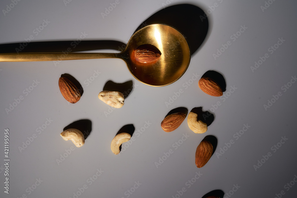 Golden spoon with cashew nuts and almonds on a gray background. Deep Shadows