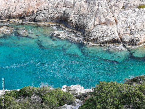 Colorful turquoise seawater seen from a cliff with trees. Amazing colors in the sea.  Narrow sea gulf between grey beige limestone rocks. 