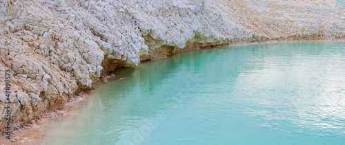 Shore with white clay close-up, turquoise azure water in pond, shallow lake with clear blue water.