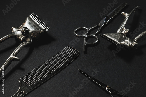 On a black surface are old barber tools. two vintage manual hair clipper, comb, hairdressing scissors. black monochrome. contrast shadows. horizontal .