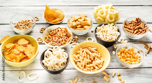 Assorted chips, popcorn, onion rings, croutons, cheese balls, cookies in bowls. unhealthy nutrition for figure, heart, skin, teeth. An assortment of fast carbohydrates. Junk food on wooden background