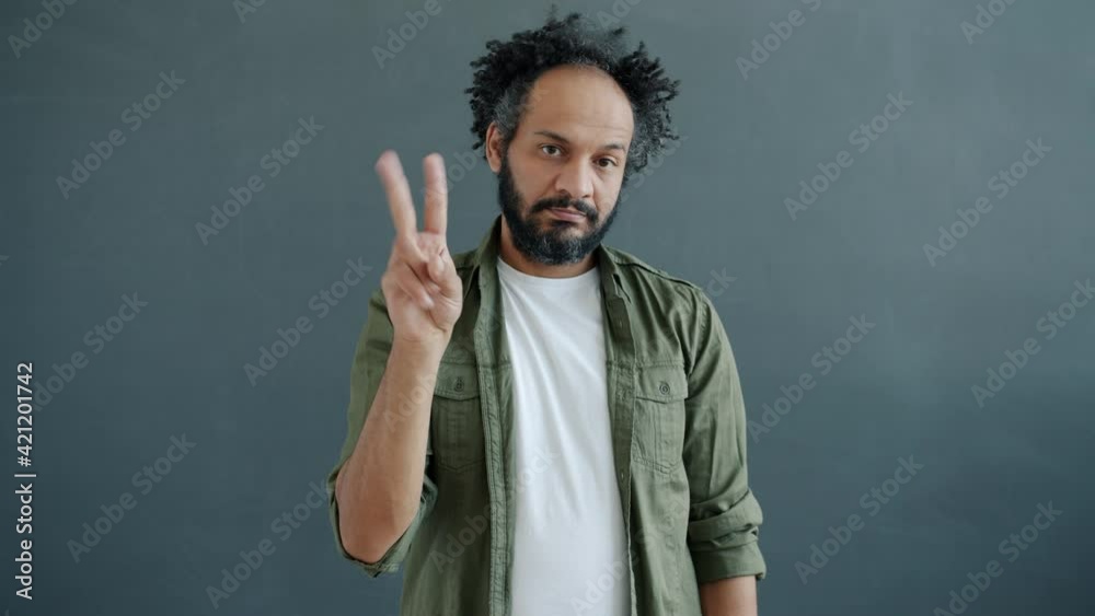 Portrait of serious mixed race man stretching arm to camera and counting with fingers from one to five standing on gray background. Deadline and emotions concept. Portrait of serious mixed race man stretching arm to camera and counting with fingers from one to five standing on gray background. Deadline and emotions concept.