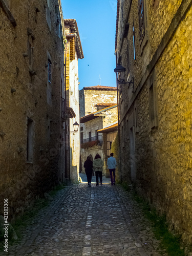Tres personas pasean por las estrechas calles con casas de piedra de la aldea medieval de Santillana del Mar, España © Franjagoher