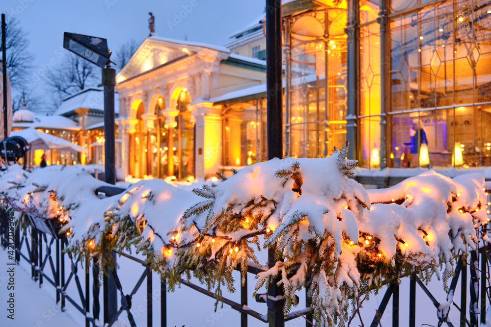 Snow-covered Christmas decorations with spruce branches and Christmas garlands on the street. Beautiful classic European architecture in the background.