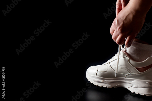 Hands tying shoelaces on sneakers. Put on sneakers on black with copy space.