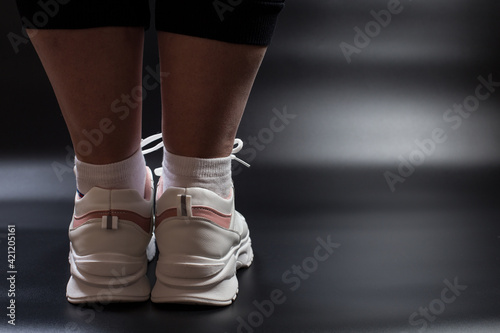 Slimming exercises. Yoga for everyone. Women's legs in sneakers. A plump girl in sneakers.