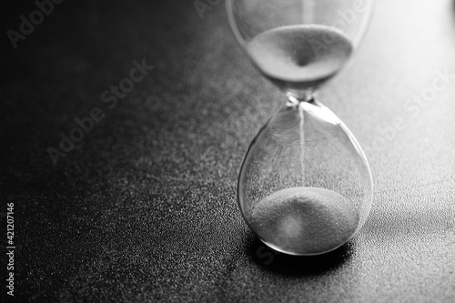 Sand passes through an hourglass measuring the travel time counting down to the deadline, black and white photo with space for text