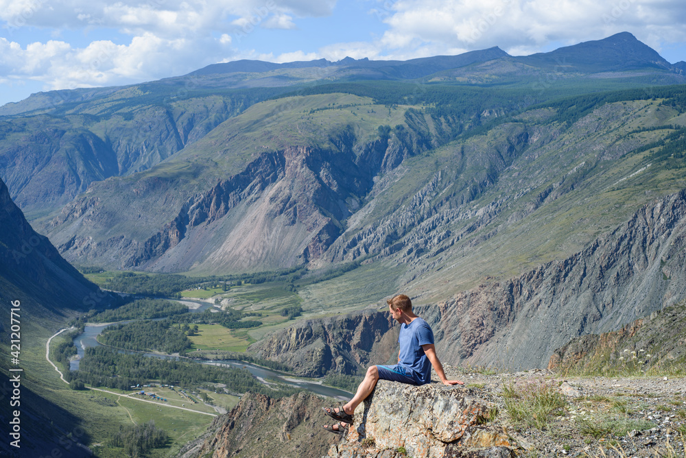 Fototapeta premium a man is resting on the edge of the mountain and enjoying the view after a long hike. Travel in the mountains.