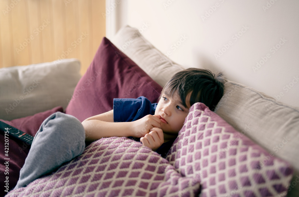 Authentic portrait Kid lying on safa biting his finger nails while watching TV, Little boy lying on couch bite his nails, Child chilling out or relaxing in living room on weekend Authentic portrait Kid lying on safa biting his finger nails while watching TV, Little boy lying on couch bite his nails, Child chilling out or relaxing in living room on weekend