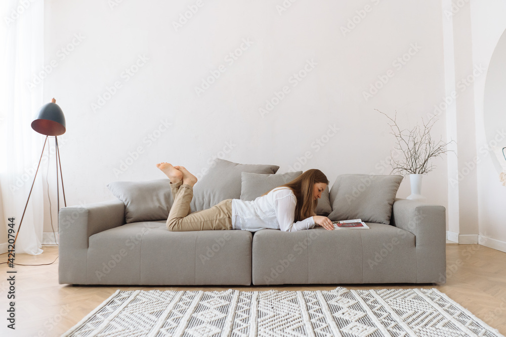 Young woman reading on the couch at home. - obrazy, fototapety, plakaty 