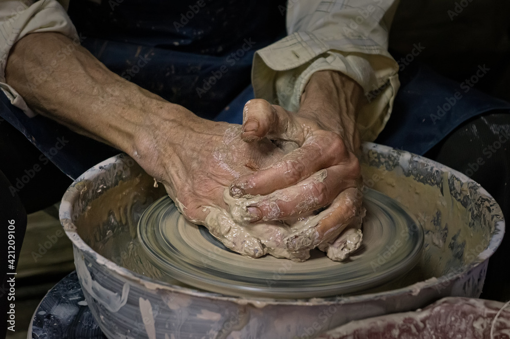 Potter at work. Old potter's hands in clay form a pot on a circle