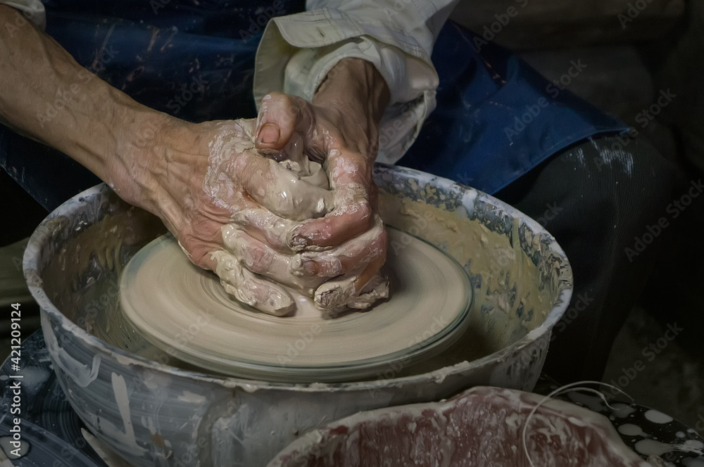 Potter at work. Old potter's hands in clay form a pot on a circle