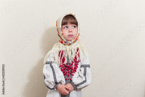 Portrait of small pretty girl in traditional ukrainian style.Young beautiful girl in a  long white national shirt and traditional scarf. Ukrainian culture, ethno style..