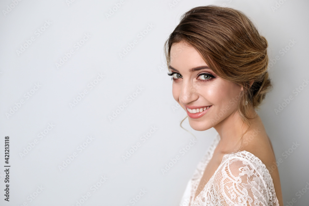 Young bride with elegant wedding hairstyle on light grey background. Space for text