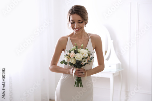 Young bride with beautiful wedding bouquet in room