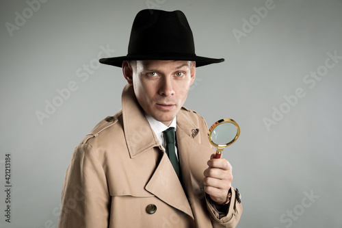 Male detective with magnifying glass on grey background photo