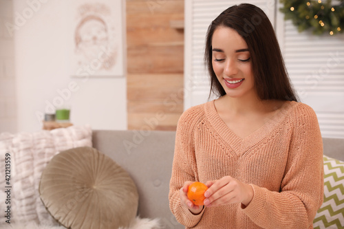 Happy young woman eating ripe tangerine at home