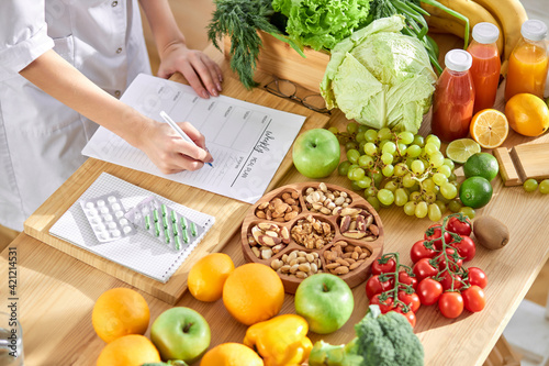Cropped dietitian, nutritionist or doctor standing by desk writing about benefits of eating fresh fruit and vegetables photo