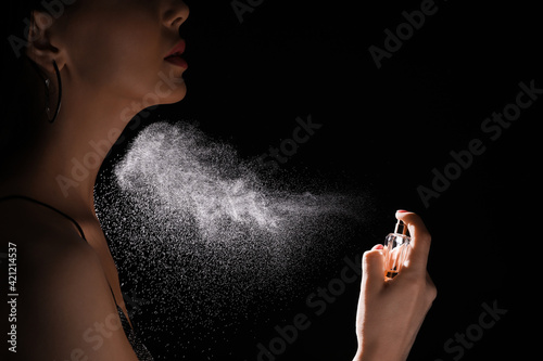 Woman spraying luxury perfume on black background, closeup photo
