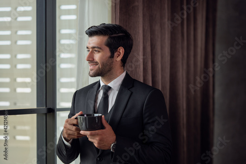 Portrait of young handsome confident businessman in suit drinking coffee