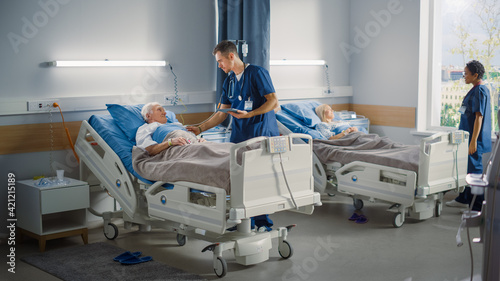 Schilderij op canvas Hospital Ward: Friendly Male Nurse Talks Reassuringly to Elderly Patient Resting in Bed
