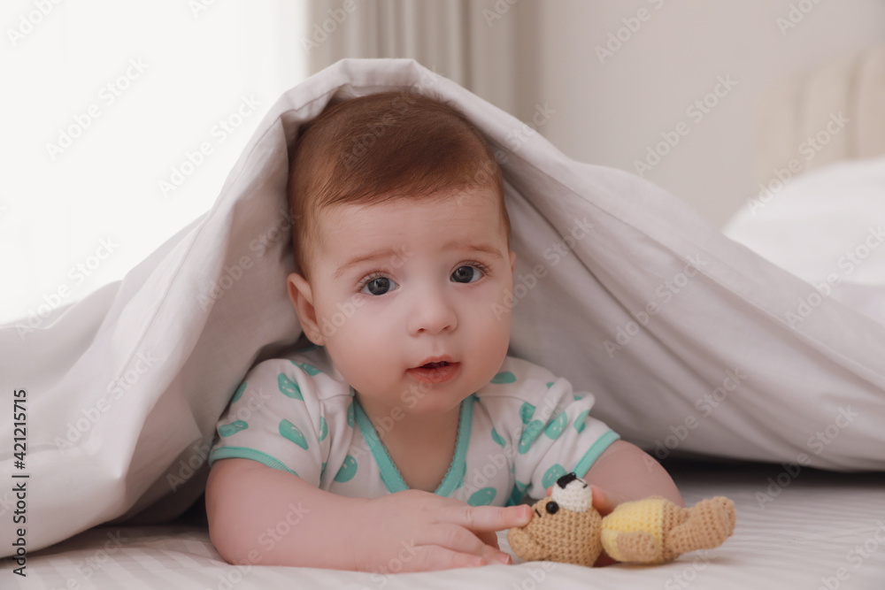 Cute little baby with toy in bed under soft blanket indoors Cute little baby with toy in bed under soft blanket indoors