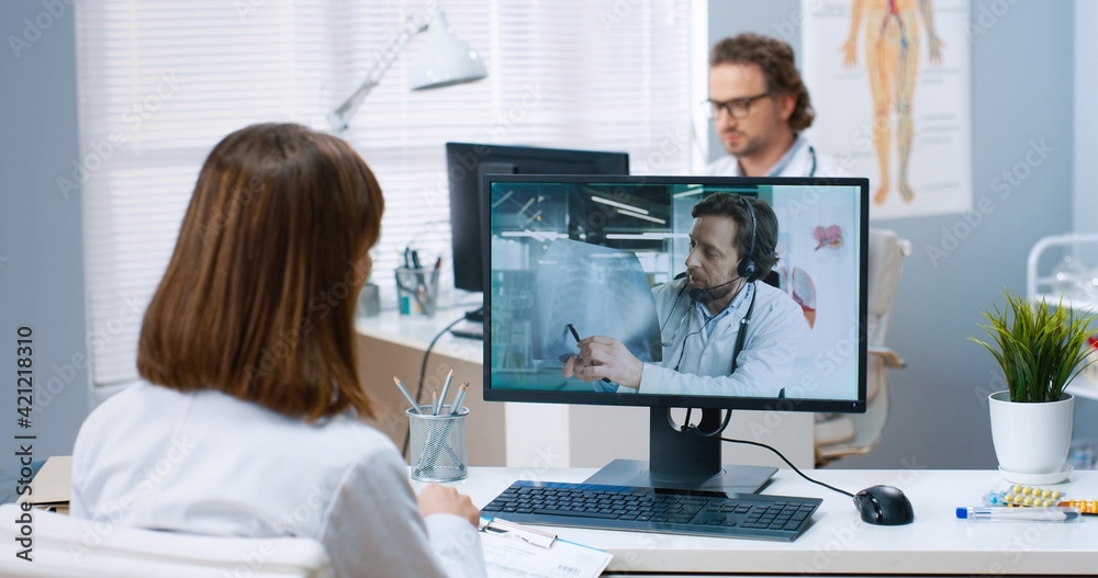 Φωτογραφία Over shoulder view of female doctor having online web conference with Caucasian male colleague on laptop sitting in hospital office