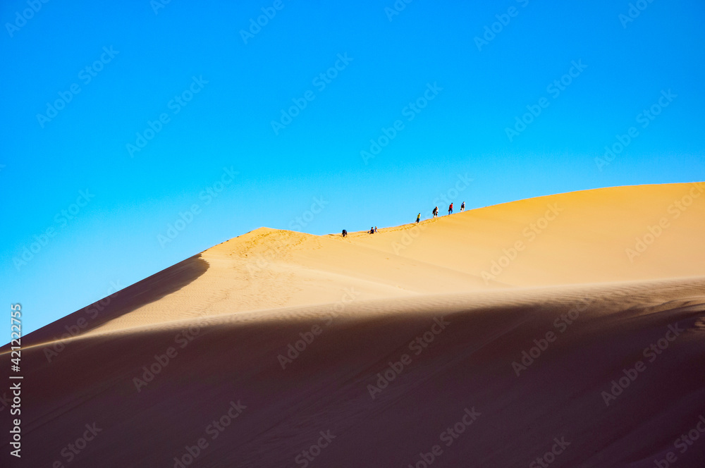 Beautiful Singing Dunes (barkhan) with silhouettes of unrecognisable tourists at the sunset at Altyn-Emel National Park in the desert in Kazakhstan