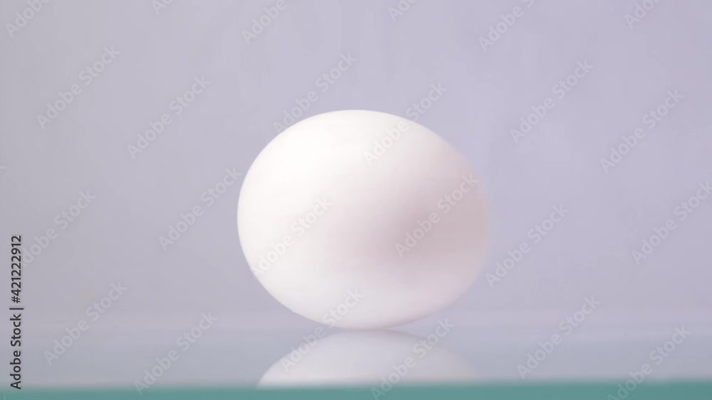 White chicken egg spinning around and rolling on a white background with beautiful reflection White chicken egg spinning around and rolling on a white background with beautiful reflection