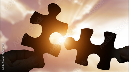 Puzzle pieces connecting with hands on sunset background