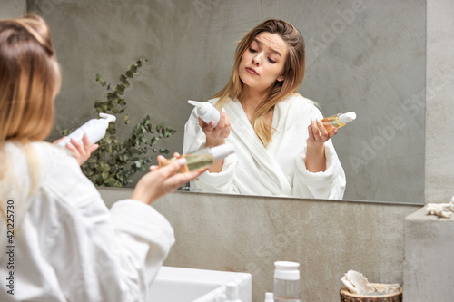 Foto adorable caucasian female selects, compares cosmetics, which one will be better