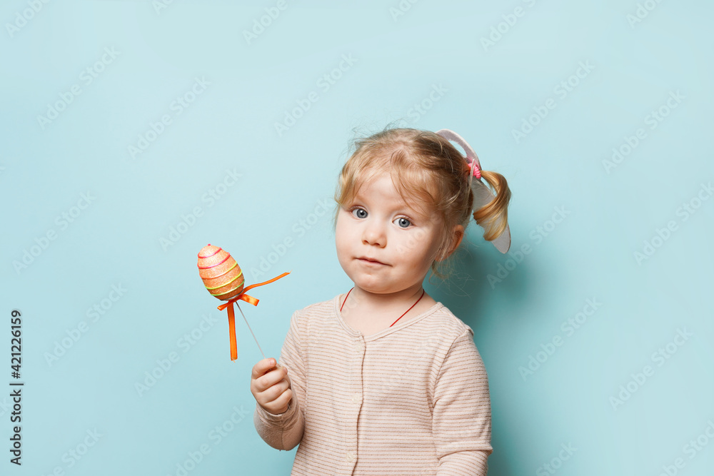 Portrait of a cute little girl dressed in Easter bunny ears holding colorful egg on blue background Portrait of a cute little girl dressed in Easter bunny ears holding colorful egg on blue background