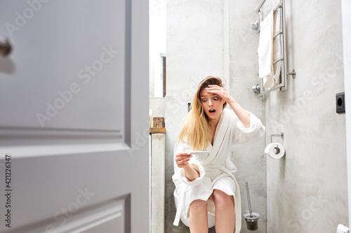 Shocked female looking at control line on pregnancy test while sitting on toilet