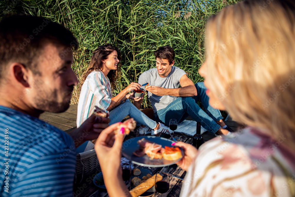 Friends having fun on picnic near a lake, sitting on pier eating and drinking wine. Friends having fun on picnic near a lake, sitting on pier eating and drinking wine.