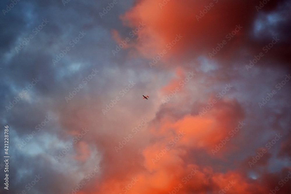 Colourful and dramatic orange and red clouds in the sky during beautiful golden hour sunset, with a small plane flying in the centre
