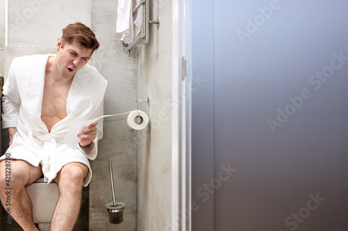 Young caucasian man suffering from hemorrhoid on toilet bowl in rest room