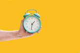 Clock. Alarm clock in a female hand on a yellow background.