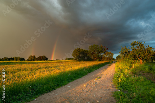 Storm cloud with rainbow, dirt road through the meadow