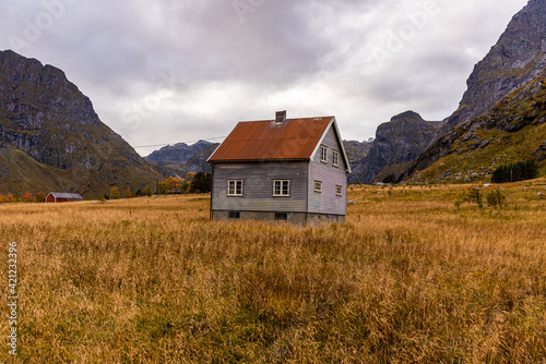 Hiking through a mountainous fjord landscape while the sun sets over the mountain peaks - landscape photo in autumn with a typical norwegian house - hiking trail to bunes beach, Reine, Lofoten, Norway