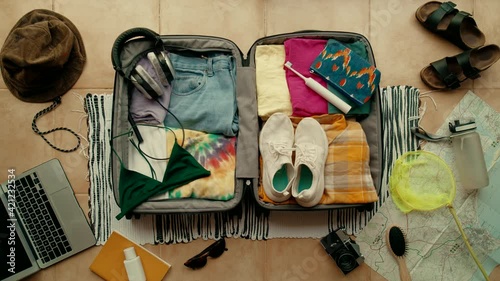 Top view of woman neatly packing and organising summer themed suitcase. Ready for vacation or holidays. Travel blogger essentials, Road trip wanderlust lifestyle. Suitcase packed and ready to go