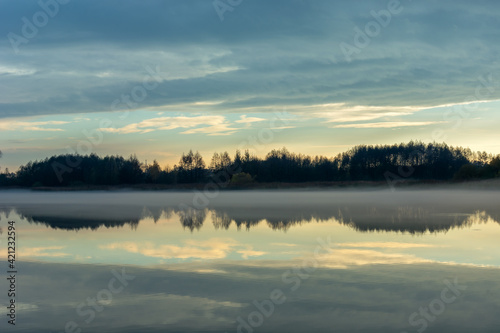 Fog over a calm lake  trees and evening clouds
