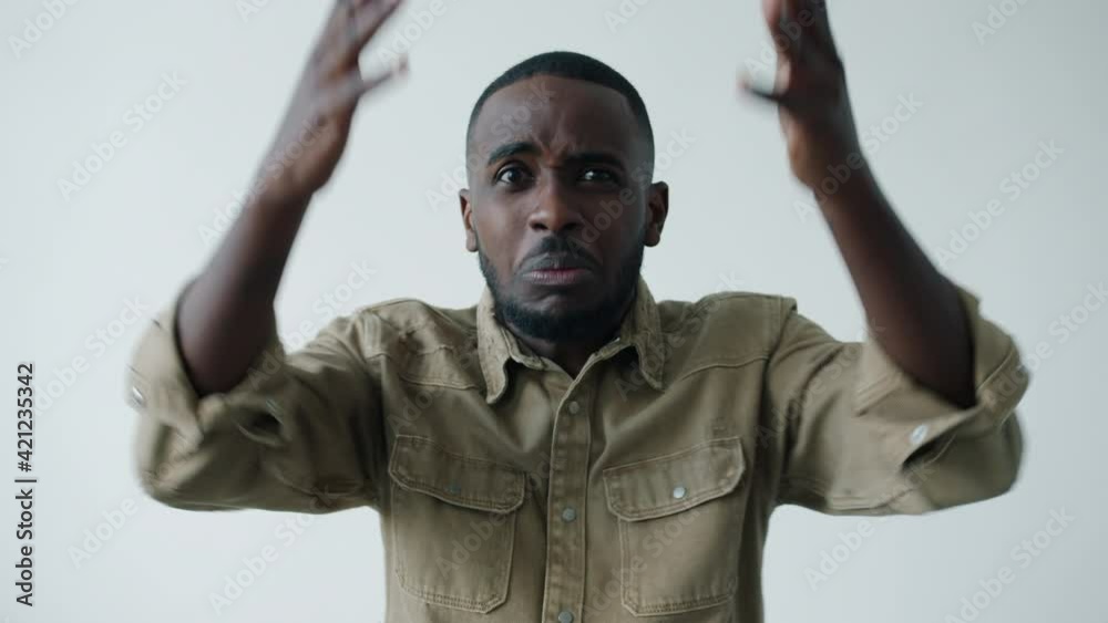 Slow motion of irritated young African American man yelling and gesturing involved in conflict standing on white background. People and emotions concept. Slow motion of irritated young African American man yelling and gesturing involved in conflict standing on white background. People and emotions concept.