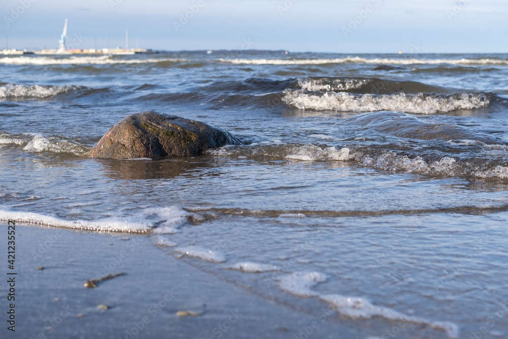 Beautiful landscape. Seashore with waves and a large stone, port on the horizon, against the blue sky. Beautiful landscape. Seashore with waves and a large stone, port on the horizon, against the blue sky.