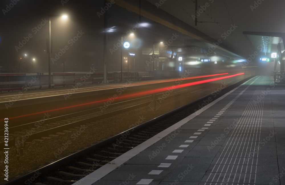 Train passing an empty platform at a railroad station during a foggy evening. Groningen, Holland.