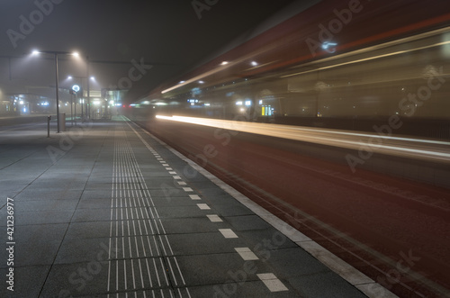 Train passing an empty platform at a railroad station during a foggy evening. Groningen, Holland. © sanderstock
