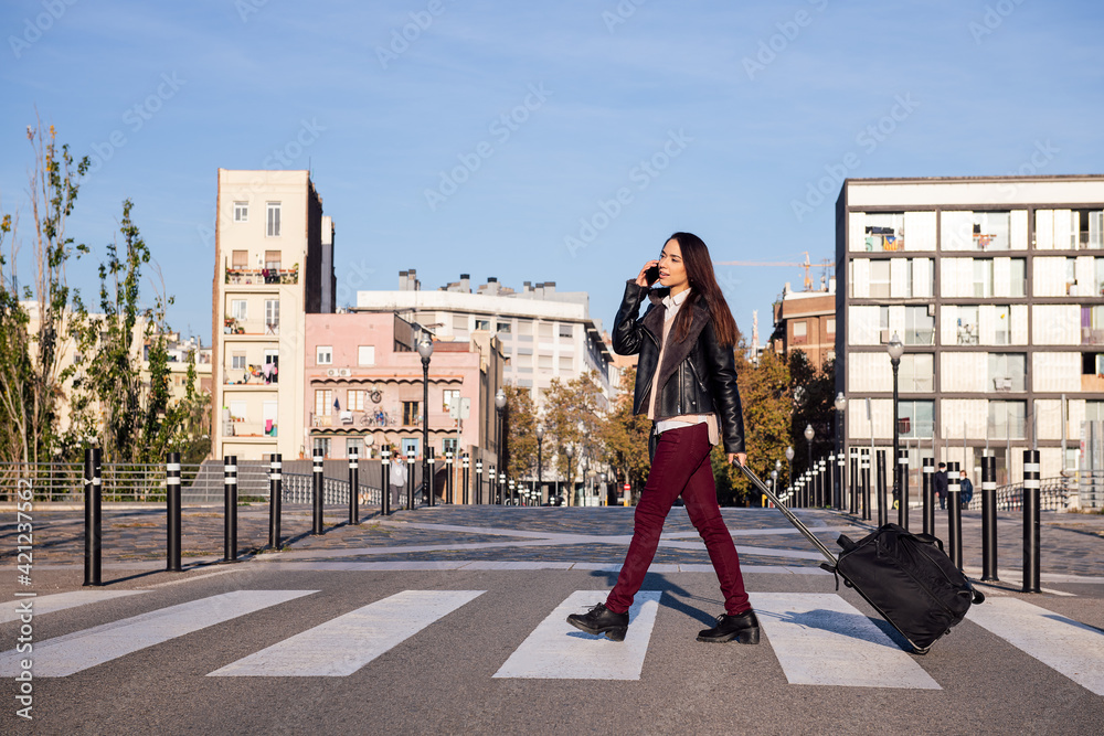 young woman pulling suitcase talking by phone